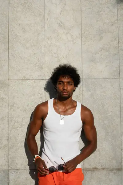  Taştan bir duvarın önünde parlak turuncu mayo ve renkli yaz giysileri giyen Brezilyalı bir model duruyor.. 