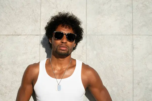  Taştan bir duvarın önünde parlak turuncu mayo ve renkli yaz giysileri giyen Brezilyalı bir model duruyor.. 