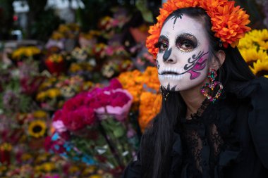 Geleneksel makyajlı bir Meksikalı Catrina, kameranın dörtte üçü açıyla çiçeklere bakıyor..