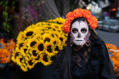 Geleneksel makyajlı Meksikalı bir Catrina canlı çiçeklerle kameraya bakıyor..