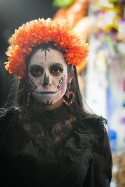  Geleneksel bir Meksikalı Catrina 'nın çarpıcı ön portresi. Güzel dekore edilmiş ve dengeli. Arka planda renkli bir şeker standı geleneksel bir dizi şekeri sergiliyor ve sahneye şenlik havası katıyor..