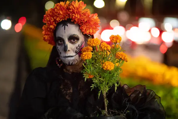 Yakın plan bir portrede Meksikalı bir Catrina canlı bir kadife çiçeği tacı takıyor ve yüzüne yakın bir cempasuchil bitkisi tutuyor. Güzellik ve geleneği harmanlıyor..