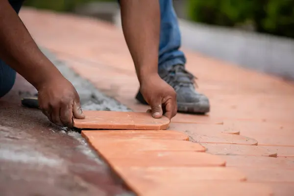 Terracotta çatı fayansını tutan işçilerin yakın çekimi, çatıya yerleştirmek için dikkatlice yerleştiriliyor. Ellere odaklanma, çatı işleminde gerekli olan hassasiyeti ve dikkati gösterir..