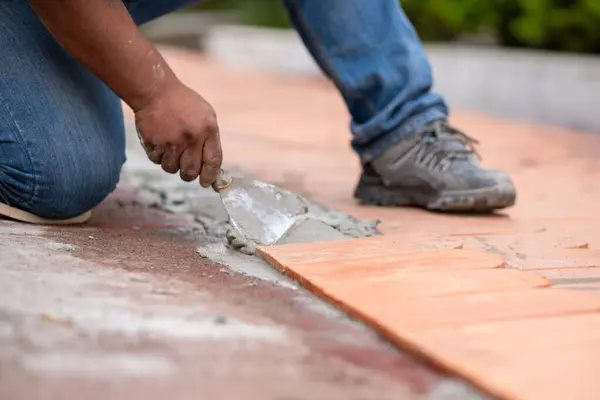 Bir sonraki terracotta çatı fayansına taze çimento sürmek için mala kullanan bir işçinin yakın çekimi. Daha önce yerleştirilmiş fayanslara odaklanarak, her bir fayansın güvenli bir şekilde yerleştirildiğinden emin olan hassasiyeti ve dikkatli çalışmayı gösteriyor.
