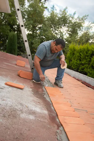 Çatı kiremitlerini yerleştirmeden önce taze çimentoyu manipüle etmek için mala kullanan bir işçinin dikey geniş açılı görüntüsü..
