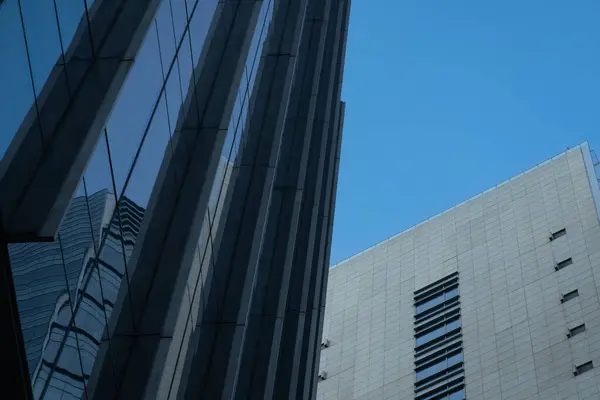 İki binanın yakın çekim görüntüsü. Birinde mavi renkli cam ön cephe, diğerinde de bej rengi tuğla var..