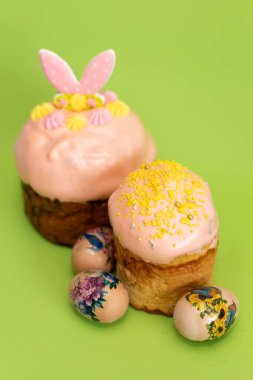 Geleneksel Ukrayna paskalya pastaları pembe krema ve şenlikli süslemelerle süslenmiş, yeşil arka planda güzel boyanmış yumurtalarla çevrili..