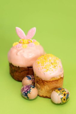 Güzel dekore edilmiş Paskalya pastaları yumuşak pembe kremalı, serpiştirmeli ve renkli yumurtalarla çevrili..