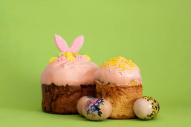 Pembe kremalı ve sarı soslu geleneksel Paskalya pastalarının parlak ışıklandırılmış kompozisyonu, sanatsal boyanmış yumurtaların yanına konur.