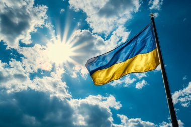 A vibrant Ukrainian flag waves proudly on a flagpole against a bright blue sky and shining sun clipart