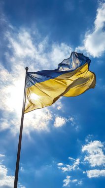 A vibrant Ukrainian flag waves proudly on a flagpole against a bright blue sky and shining sun clipart