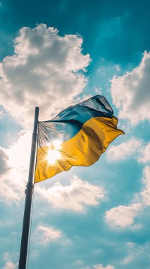 A vibrant Ukrainian flag waves proudly on a flagpole against a bright blue sky and shining sun clipart