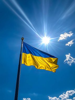 A vibrant Ukrainian flag waves proudly on a flagpole against a bright blue sky and shining sun clipart