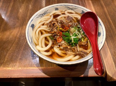 Tahta bir masada servis edilen dilimlenmiş biftekli Udon ramen eriştesi.