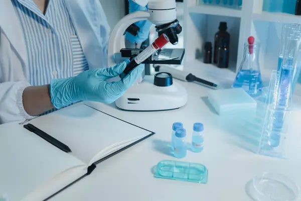 Kimyager kandaki kimyasalları araştırmak için mikroskop kullanıyor. Bilim adamı laboratuvarda kimyasallarla deney yapıyor. Kimyager test tüplerindeki kimyasalları kimyasal reaktörlerle ayırıyor.,