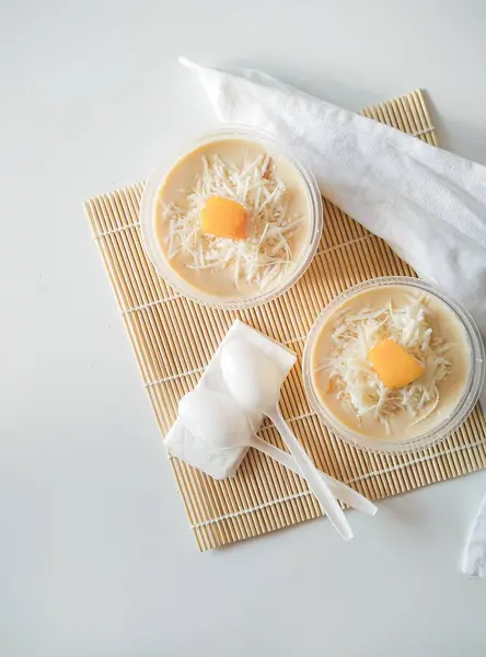 Süt kremalı iki fincan mango tatlısı ve bambu soslu rendelenmiş peynir ve beyaz arka planda mango garnitürü.