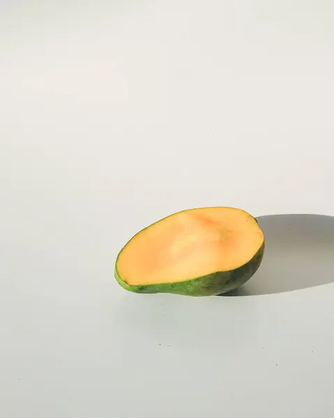 Beyaz arka planda mango gölgesi olan yarım kesilmiş mango meyvesi.
