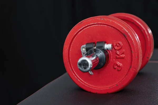 Dumbbell with red weights on a black weight training bench ready to use on a black background