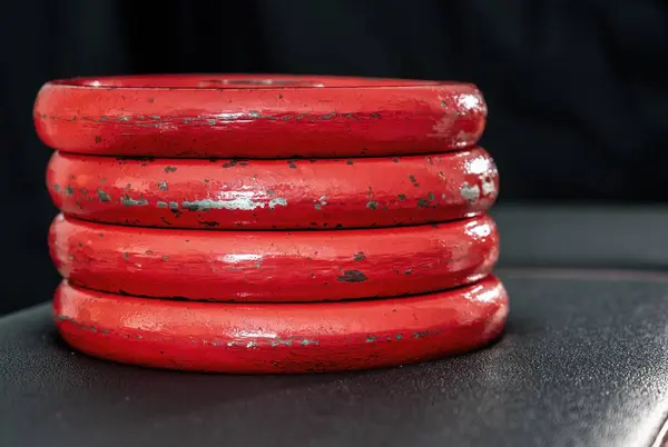 Stack of red weights on a black weight training bench ready to use on a barbell or dumbbell on a black background
