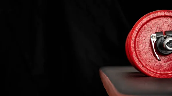 Dumbbell with red weights on a black weight training bench ready to use on a black background