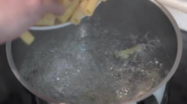Bir adamın elinin yavaş çekimde pişirilmesi için kaynar suya makarna dökmesi.