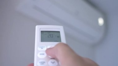 Bir adamın eli klimayı açmak için düğmelere basar ve 25 santigrat dereceye ayarlar.