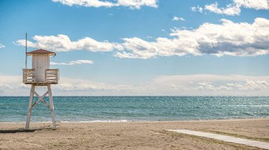 Sakin bir günde sahildeki cankurtaran kulesi ve bulutlu mavi gökyüzü.