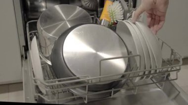 Bir adamın eli bulaşık makinesini boşaltıyor, tabakları alt raftan topluyor. Video, günlük ev işlerinin temiz ve düzenli bir mutfağı gösteren bir anını yakalıyor.