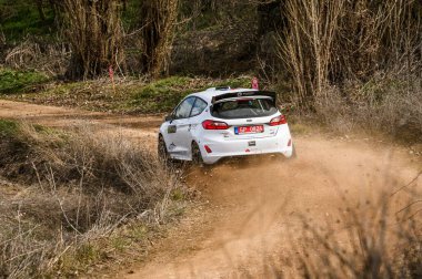 Madrid, İspanya; 02-15-2025: Beyaz Ford Fiesta ralli arabası Alcarria Madrilena Rallisi 'nde çakıllı bir virajda hızla giderken tozu dumana katıyor. Devingen bir aksiyon sahnesi off-road yarışının heyecanını yakalıyor.