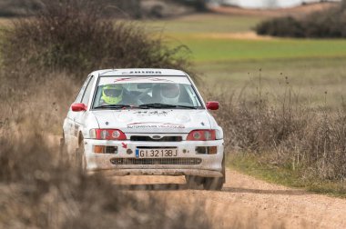 Madrid, İspanya; 02-15-2025: Beyaz Ford Escort RS Cosworth ralli arabası toprak ve çakıl pistinde toz kaldırma yarışı yapıyor