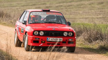 Madrid, İspanya; 02-15-2025: Klasik kırmızı BMW 325i E30 rali arabası virajlı toprak yollarda hızla toz kaldırıyor