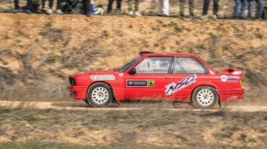 Madrid, İspanya; 02-15-2025: Klasik kırmızı BMW 325i E30 ralli arabası halkın tetikte olduğu bir mitingde virajlı toprak yollarda yarışıyor