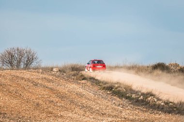 Madrid, İspanya; 02-15-2025: Klasik kırmızı BMW 325i E30 rali arabası virajlı toprak yollarda hızla toz kaldırıyor