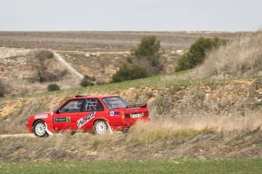 Madrid, İspanya; 02-15-2025: Klasik kırmızı BMW 325i E30 rali arabası virajlı toprak yollarda hızla toz kaldırıyor