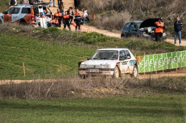 Madrid, İspanya; 02-15-2025: Iconic Peugeot 205 GTI, canlı bir rali kutlamaları sırasında, etkinlikte güvenliği sağlayan ihtiyatlı acil durum personeli altında toprak pistte kükrüyor