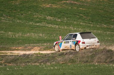 Madrid, İspanya; 02-15-2025: İkonik Peugeot 205 GTI bir rali kutlamaları sırasında tozlu bir ufka doğru geri çekilirken, toprak yolda hızlanıyor