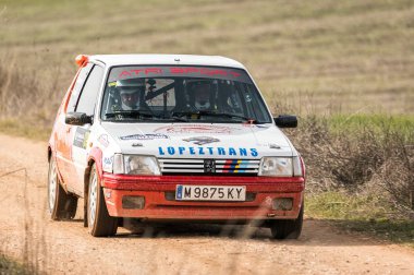 Madrid, İspanya; 02-15-2025: Peugeot 205 'in bir rallide toprak pist boyunca yarışırken ön görüntüsü, ham güç, hassasiyet ve heyecan verici motor sporu hareketi sergiliyor.
