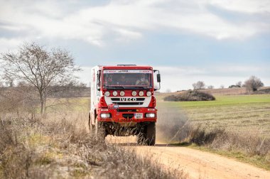 Madrid, İspanya; 02-15-2025: Kırmızı ve beyaz Iveco MP190E4W ralli kamyonu sert bir off-road motorsporu yarışında toz püskürterek engebeli bir toprak pist boyunca saldırıyor