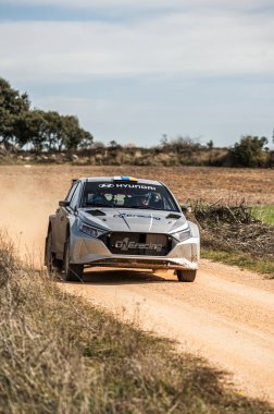 Madrid, İspanya; 02-15-2025: Bir Hyundai i20N Rally2 tam bir rekabet içinde toprak yolda hız yaparak doğal bir arazide tozu tekmeliyor. Müthiş bir ralli heyecanı.