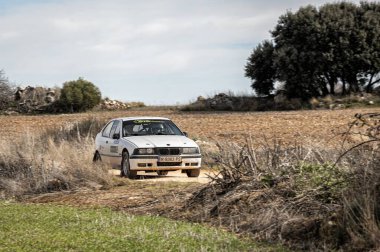 Madrid, İspanya; 02-15-2025: Engellerin etrafında manevra yapan engebeli bir toprak rali sahnesinde beyaz bir BMW 316i E36 gücü. Klasik rali arabası dayanıklılık ve hız için yapılır.
