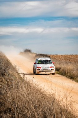 Madrid, İspanya; 02-15-2025: Ford Escort RS Corsworth, yoğun mavi gökyüzü olan bir günde toprak yolda ilerleyen ve toz kaldıran klasik bir araç
