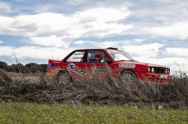 Madrid, İspanya; 02-15-2025: Bir BMW 325i E30 serisi rali arabası bir çakıl mitinginin bir safhasında bir bahar günü kırsal bir pistte sürüyor.