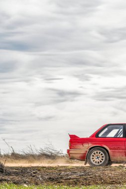 Bulutlu gökyüzüne sahip toprak bir yolda hareket halindeki kırmızı ralli arabasının arka görünümü; gezici bir duvar kağıdı olarak ideal