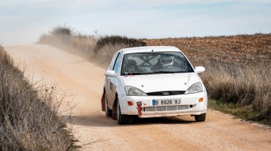 Madrid, İspanya; 02-15-2025: Bir Ford Focus 1.6 rali arabası tozlu bir pistte parlayarak, adrenalin dolu off-road motorsporları yarışında şiddetli bir şekilde rekabet ederken ardında toz bulutu bırakır