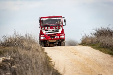 Madrid, İspanya; 02-15-2025: Kırmızı ve beyaz Iveco MP190E4W ralli kamyonu sert bir off-road motorsporu yarışında toz püskürterek engebeli bir toprak pist boyunca saldırıyor