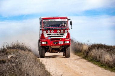 Madrid, İspanya; 02-15-2025: Kırmızı ve beyaz Iveco MP190E4W ralli kamyonu sert bir off-road motorsporu yarışında toz püskürterek engebeli bir toprak pist boyunca saldırıyor