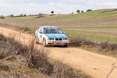 Madrid, İspanya; 02-15-2025: Mavi ve beyaz bir BMW 323i E36 bir çakıl rali pistinde geziniyor, kırsal alanda hızla toz topluyor