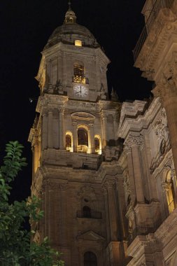 Malaga Katedrali 'nin aydınlık çan kulesinin gece görüntüsü, siyah gökyüzü altında ayrıntılı Rönesans mimarisini sergiliyor.