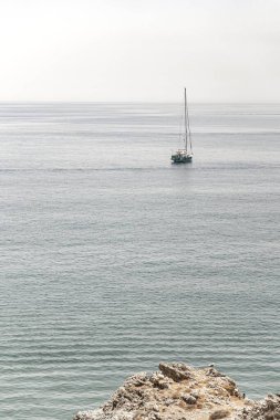 Açık ufukta turkuaz bir denizde yüzen yelkenli. Sisli bir gökyüzünün altında renkli paraşütlü bir paraşüt.