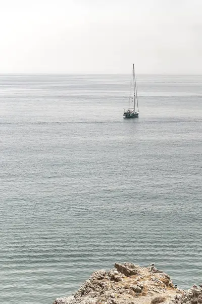 Açık ufukta turkuaz bir denizde yüzen yelkenli. Sisli bir gökyüzünün altında renkli paraşütlü bir paraşüt.